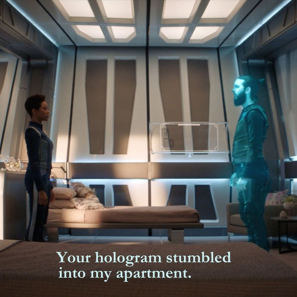 A screenshot of Michael Burnham in her quarters talking to a hologram of Ash Tyler. The words "Your hologram stumbled into my apartment" are at the bottom of the shot.