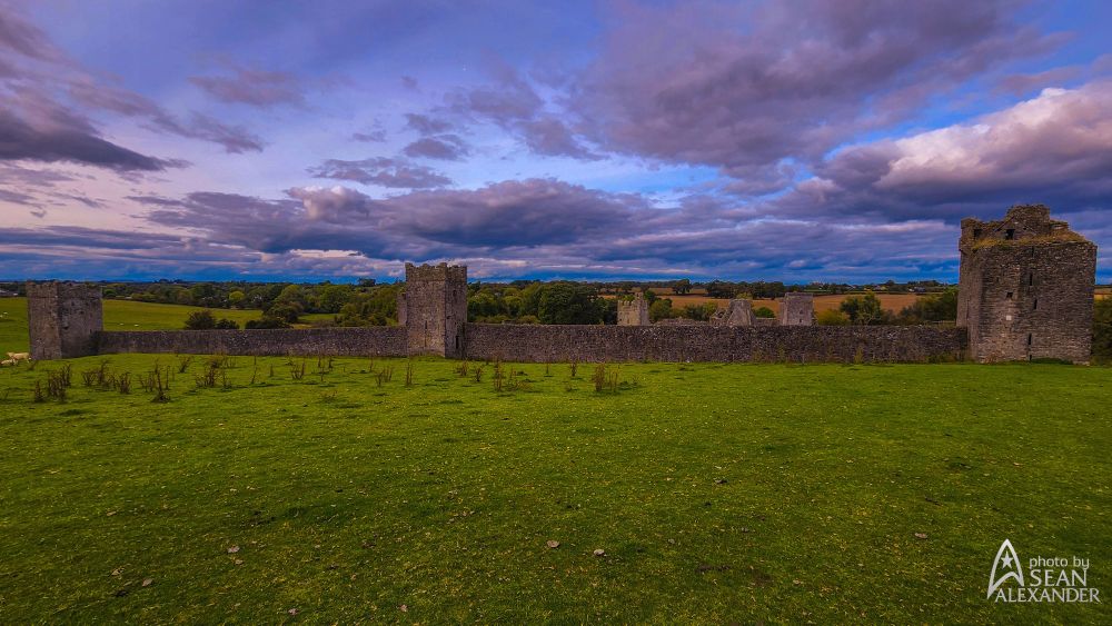 Partly cloudy skies float over the expansive stone walls and towers of Kells Priory.