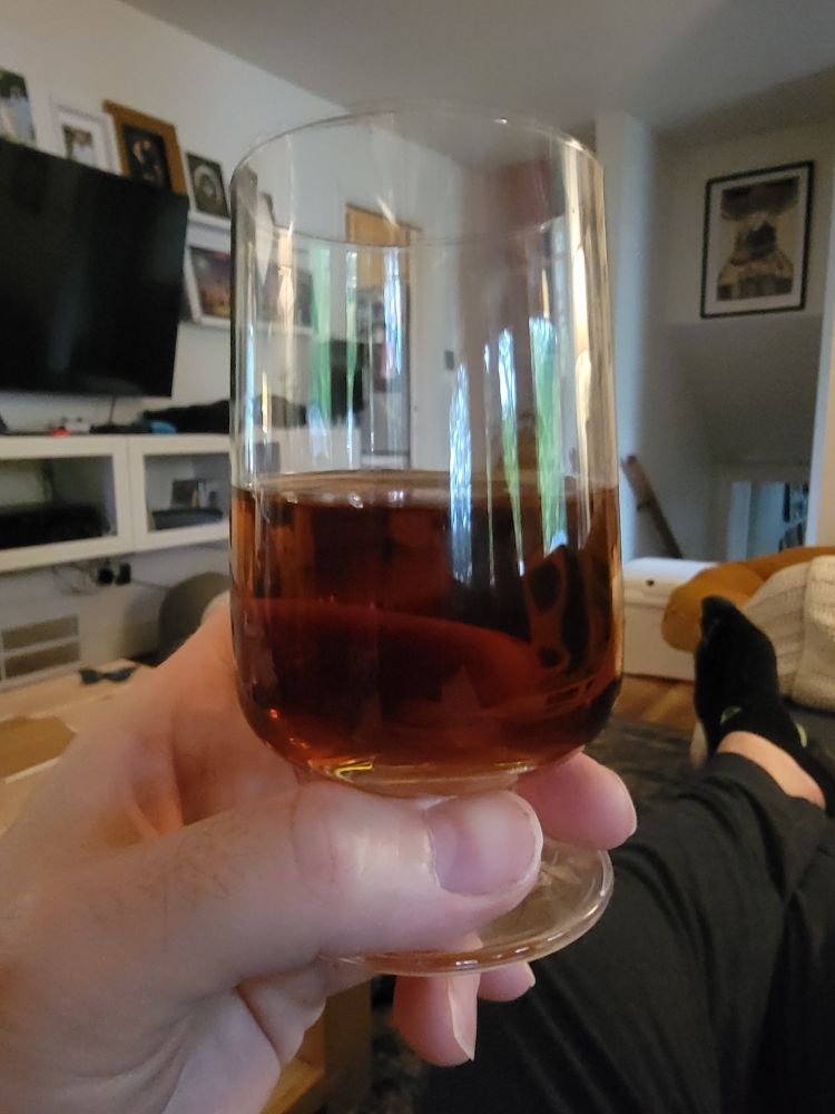 A tasting glass of a clear, brown beverage, the color of caramelized onions.  In fact it is wine made from onions, held by a reclining man (not pictured.)