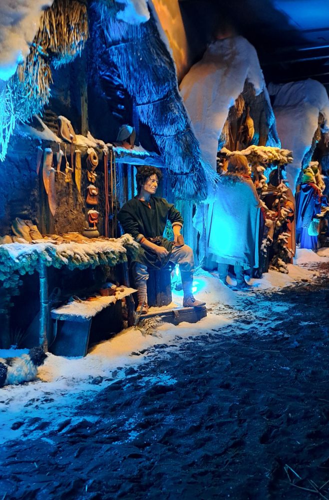 The leatherworker sits outside his house on the Jorvik Viking Centre reconstruction of the Viking settlement in York, UK. There is snow all around, icicles hang from the roof and evergreen boughs decorate the houses to portray how the Norse settlers of York survived the winter, with blue lighting to enhance the feel of a cold day in 960AD. 