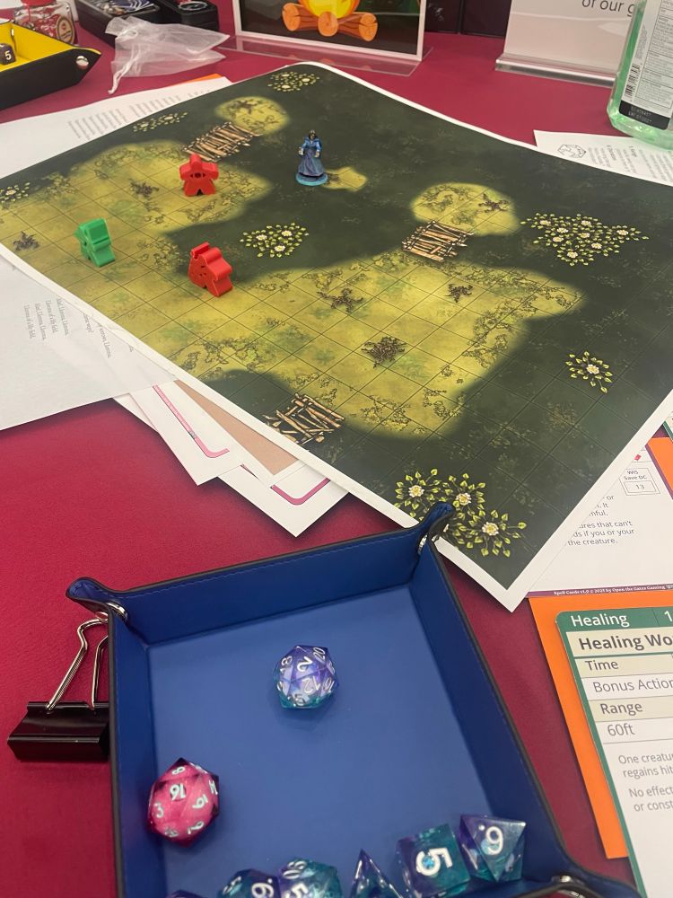 Table with an array of character sheet materials, grid map, D&D miniatures including a custom La Llorona figure, dice tray, and polyhedral dice. 