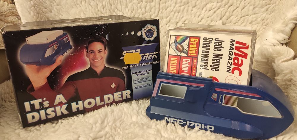 Auf einem weißen Kunstfell liegt links eine Schachtel und rechts ein Diskettenhalter. Der Diskettenhalter entspricht in der Grundform dem aus ST:TNG bekannten Shuttle und ist Dunkelblau mit aufgeklebten Fenstern/Verzierungen. Er ist oben offen. Darin stehen mehrere CD. Die Vorderste ist eine Leser-CD des Mac Magazins. Die Schachtel zeigt einen Jungen in einer roten ST:TNG Kapitäns-Uniform der den Diskettenhalter, gefüllt mit 3,5 Zoll Disketten hochhält.