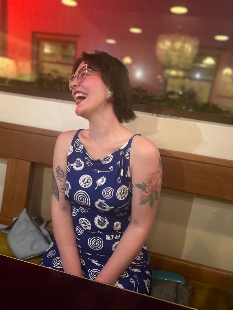 a picture of me laughing, i’m wearing a blue dress and i have v cute tattoos