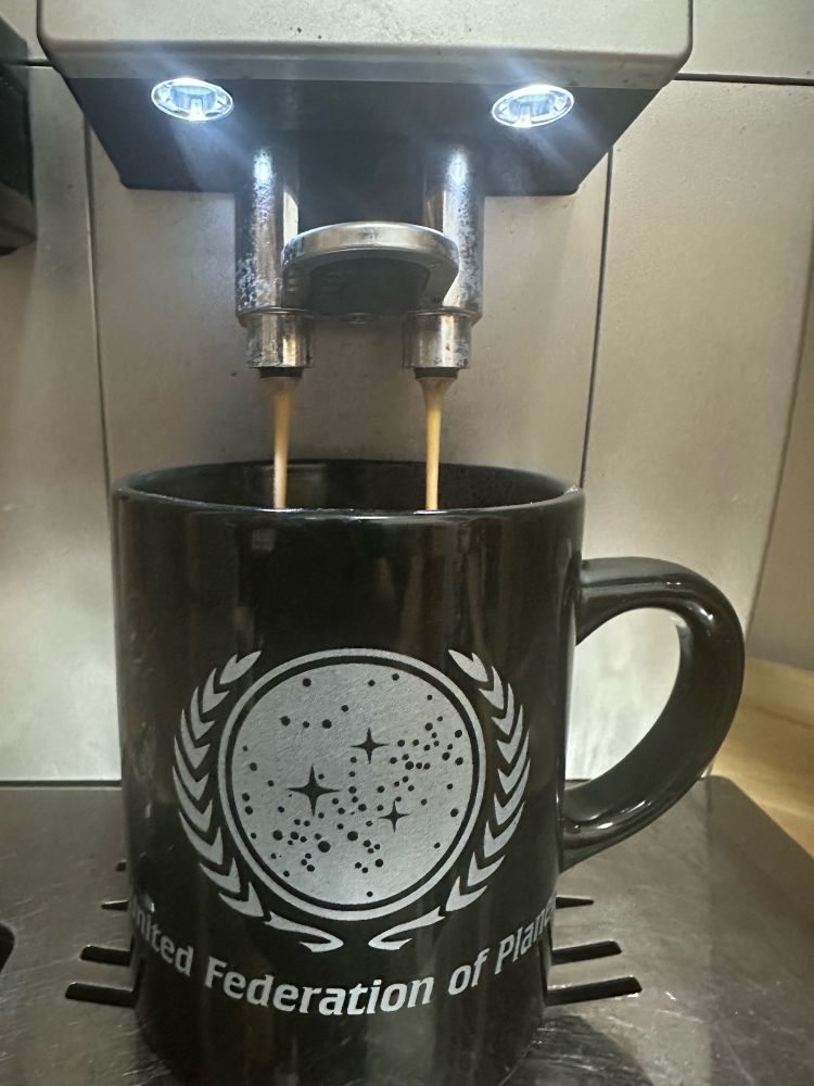 Kaffeetasse der Vereinten Föderation der Planeten aus Star Trek unter einem Kaffeevollautomaten, die gerade mit Kaffee befüllt wird.
