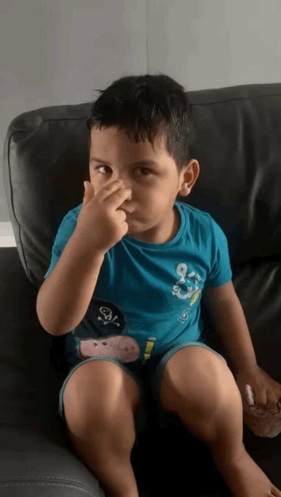 a little boy sitting on a couch holding his nose