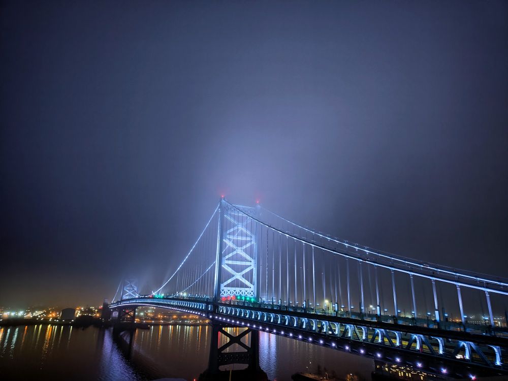 Epic shot of the Ben Franklin bridge at night glowing in the low cloud cover