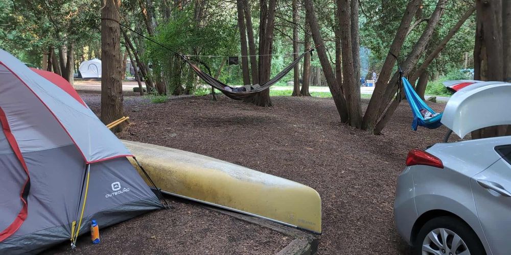 Photo of a campsite featuring a tent, 2 hammocks, and a canoe