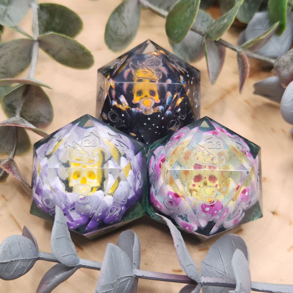 A collection of 3 handmade Jumbo D20's. Each with a unique 3d modeled skull lotus inclusion inside. Handpainted with different lotus flower color designs.