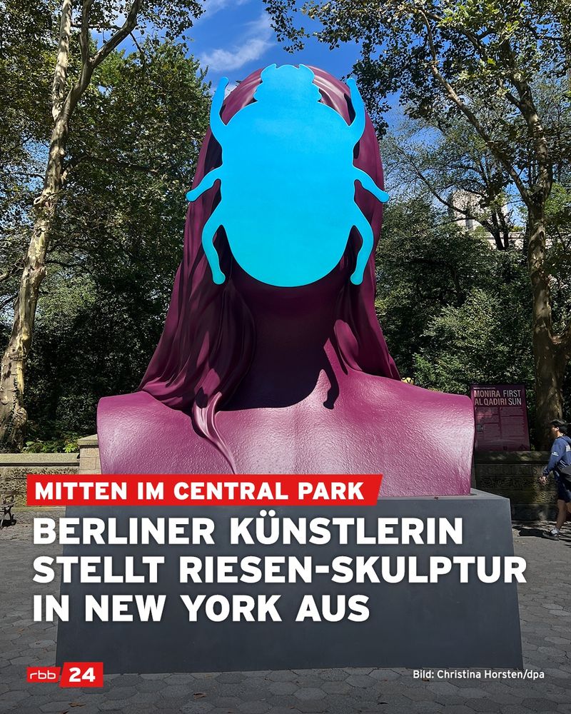 Große Skulptur im Central Park, New York: Ein purpurfarbenes, stilisiertes Frauenbüsten-Porträt mit langen Haaren. Vor dem Gesicht ist eine leuchtend blaue Käferform angebracht, die das Gesicht vollständig verdeckt. Bäume und Spaziergänger:innen im Hintergrund. Text im Bild: „Mitten im Central Park – Berliner Künstlerin stellt Riesen-Skulptur in New York aus“. Quelle: rbb24 / Foto: Christina Horsten, dpa.