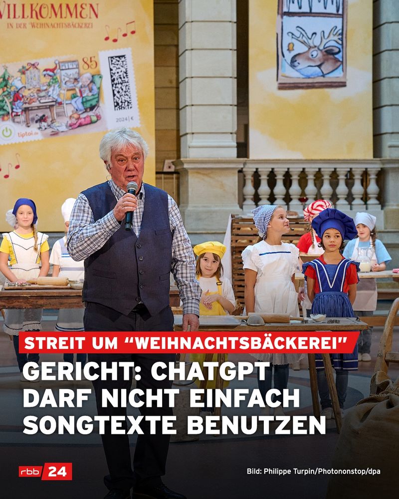Ein älterer Mann steht mit Mikrofon auf einer Bühne und spricht, hinter ihm stehen mehrere Kinder in bunten Bäcker- und Weihnachtskostümen. Im Hintergrund hängt ein großes gelbes Plakat mit der Aufschrift „Willkommen in der Weihnachtsbäckerei“ und einer Briefmarkenabbildung. Auf dem Bild steht in roten und weißen Balken: „Streit um ‘Weihnachtsbäckerei’ – Gericht: ChatGPT darf nicht einfach Songtexte benutzen.“ Unten links ist das rbb24-Logo eingeblendet.
