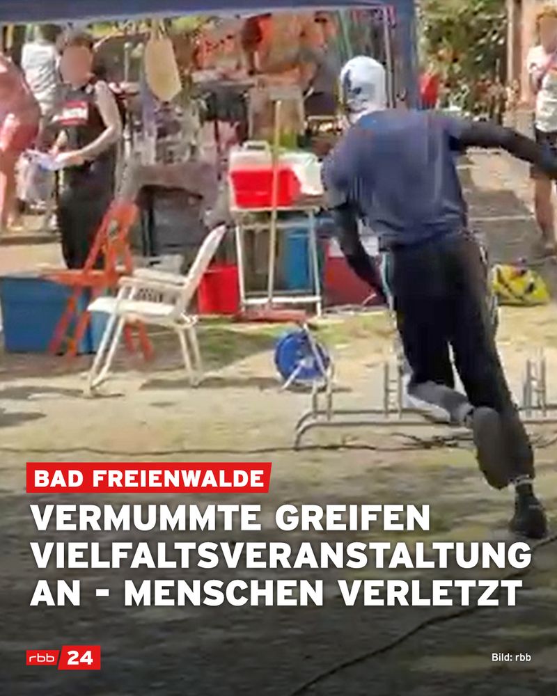 Bei einer Veranstaltung im Freien mit Marktständen und Besuchern rennt eine vermummte Person in dunkler Kleidung und Sturmhaube auf die Szenerie zu. Im Vordergrund sind umgestürzte Stühle und ein Kabeltrommelwagen zu sehen. Im Hintergrund schauen Menschen erschrocken oder weichen aus. Text im Bild: „Bad Freienwalde – Vermummte greifen Vielfaltsveranstaltung an – Menschen verletzt“. Quelle: rbb.