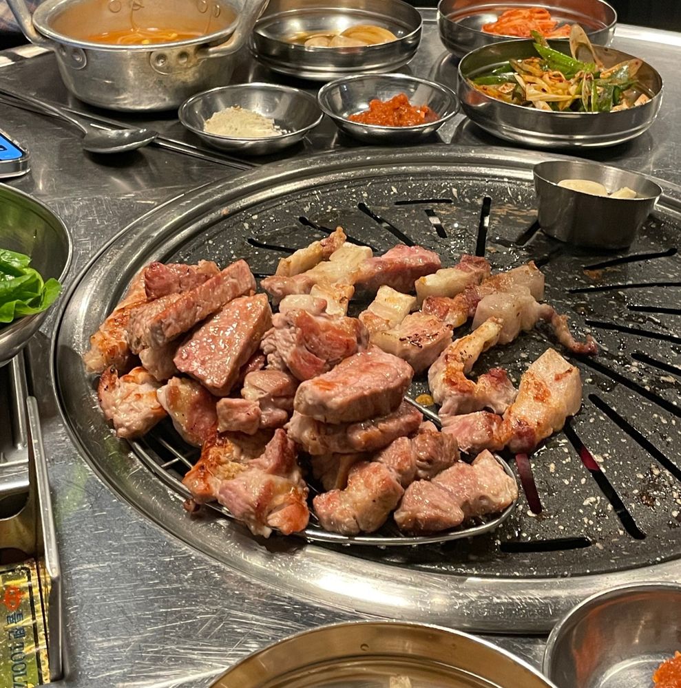 동그란 불판 위의 한켠에 고기가 산처럼 쌓여있음