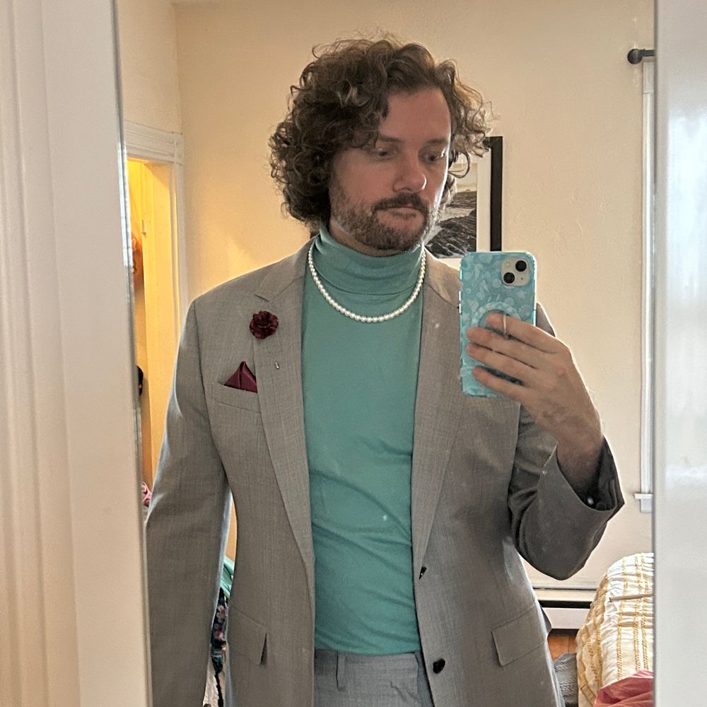 Matt wearing a green turtleneck under a grey suit with a pearl necklace
