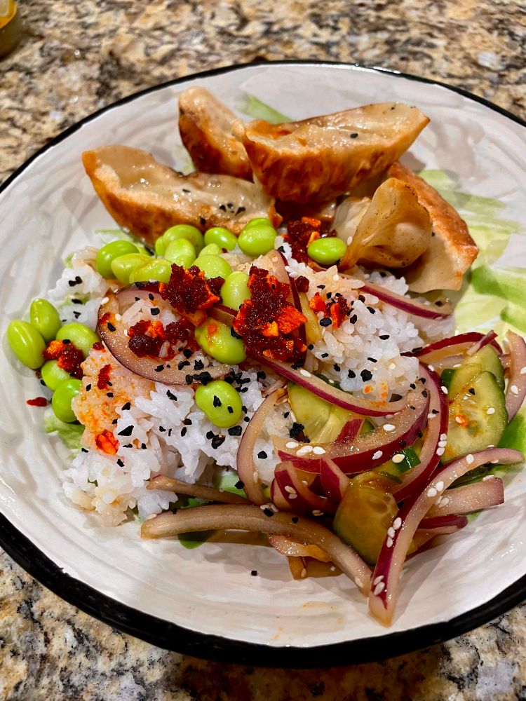 a plate of fried potstickers white rice edamame cucumbers red onion and crunchy chili garlic 
