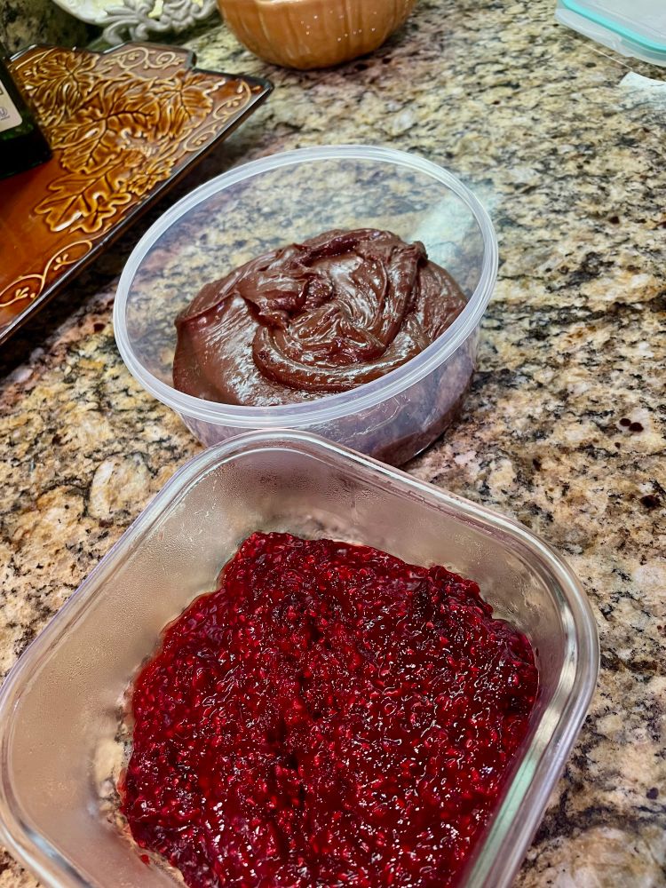 A container of raspberry filling next to a container of chocolate frosting 