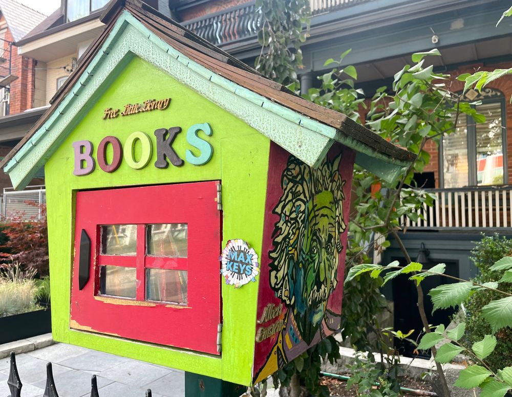 A little free library on the side of the road. Painted in bright green and red with multicoloured letters and a colourful portrait of Albert Einstein on the side. 