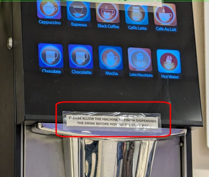 A fancy-looking coffee machine with a touch screen offering many different versions of coffee and/or chocolate.

A laminated notice has been stuck to it, saying "PLEASE ALLOW THE MACHINE TO FINISH DISPENSING THE DRINK BEFORE MOVING THE CUP AWAY"