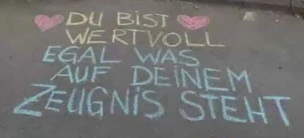 Text mit Kreide auf Schulhof: „Du bist wertvoll - egal was auf deinem Zeugnis steht“ eingerahmt von zwei roten Herzen 