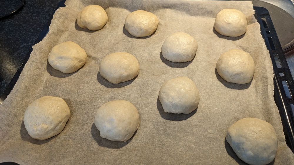 11 runde Teiglinge liegen auf einem mit Backpapier ausgelegtem Backblech und warten darauf, bis sie in den Ofen dürfen.