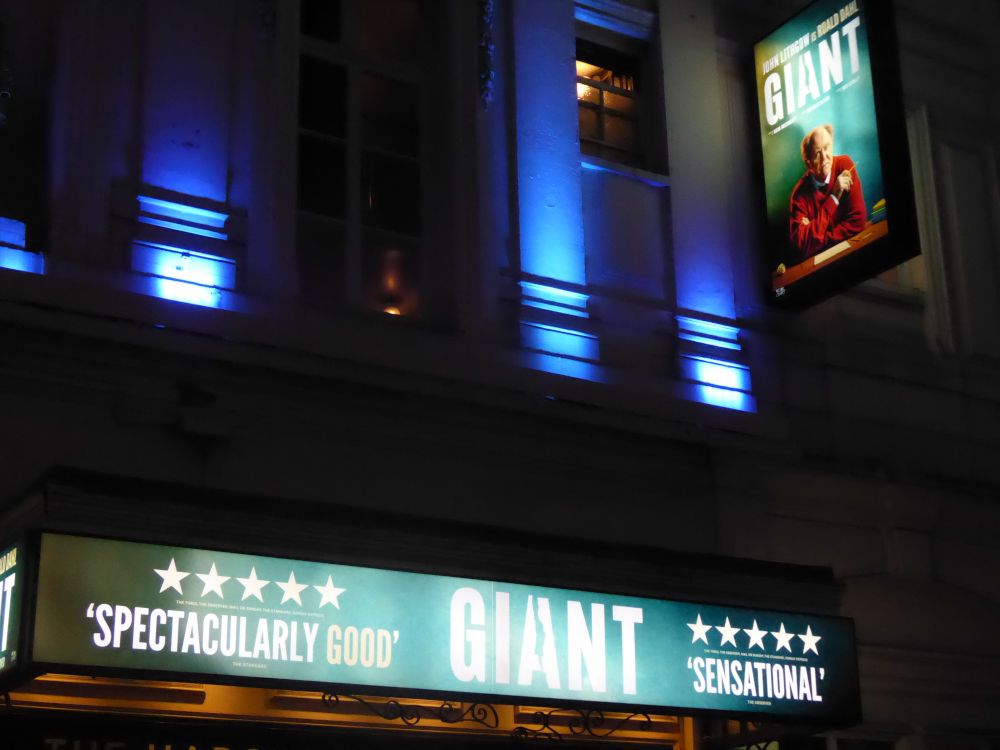 Front of theatre with illuminated hoarding and illuminated poster for Giant. Evening.