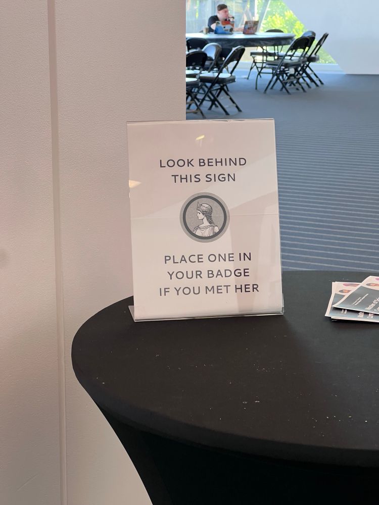 A sign that says: "Look behind this sign, place one on your badge if you met her"