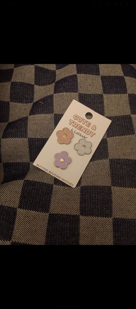 A photo of heavy weight dark wash denim featuring a checkerboard pattern ; there are 3 enamel flower shaped buttons in pink, blue, and purple set on top of the fabric. 