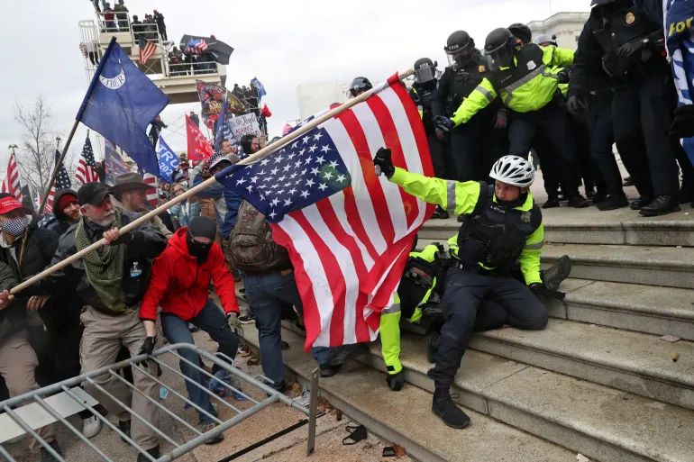The riot on the Capitol steps. An insurrectionist attacks a police officer with an American flag as the officer tries to defend himself. 