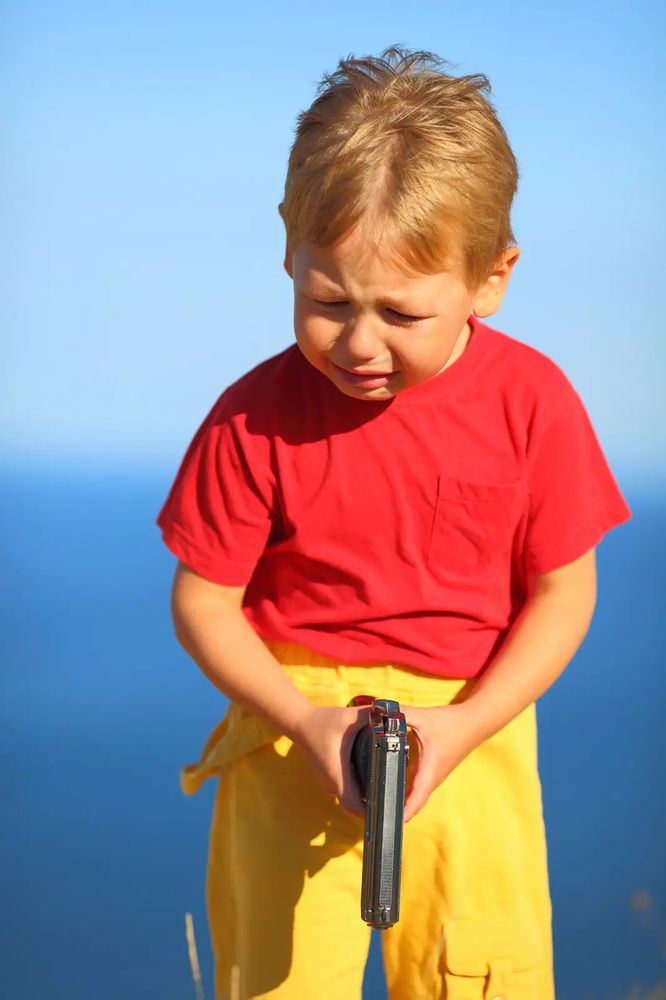 A picture of a toddler holding a gun and looking sad
