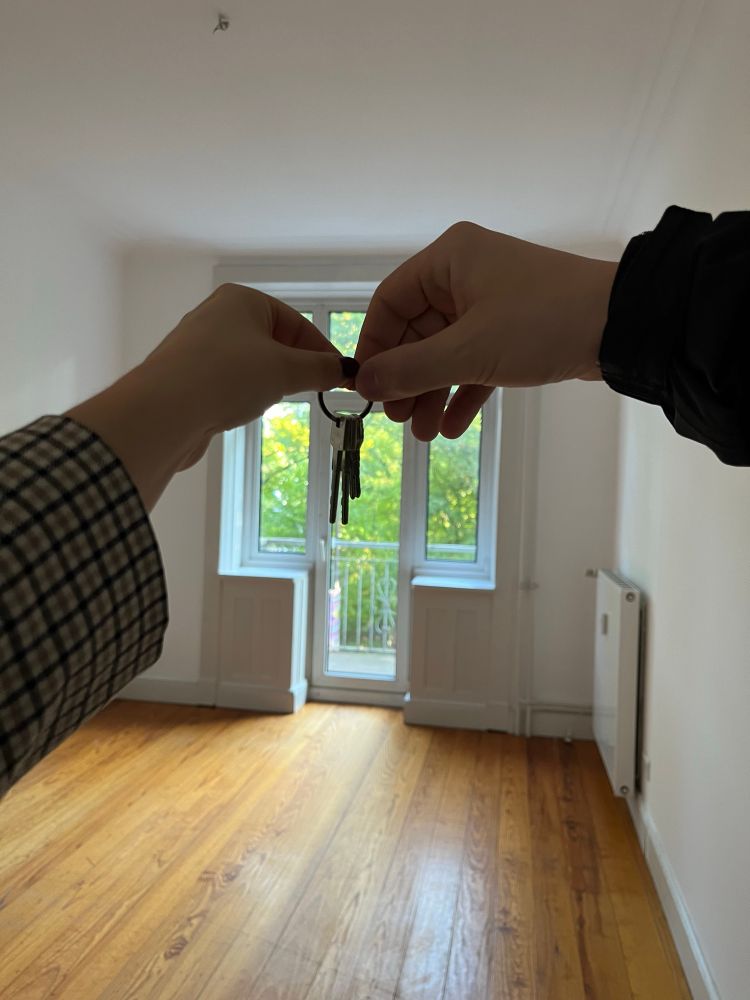 zwei hände halten einen wohnungsschlüssel. Im
Hintergrund ist ein Raum mit Holzboden