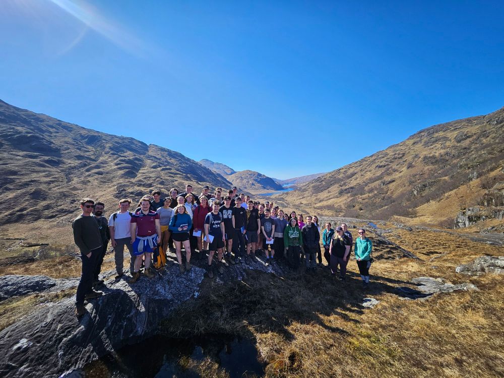 A picture of 45 students standing on a rock outcrop in Scotland with blue sky and a valley in the background