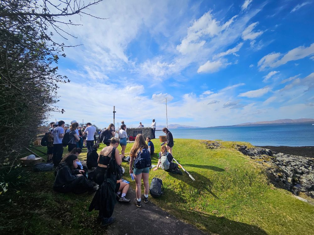 Students gathered and a grass bank beside the beach