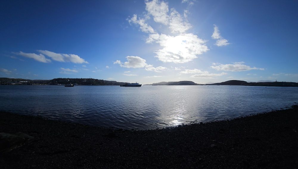 A picture of the calm sea at Oban with blue sky and an island in the distance