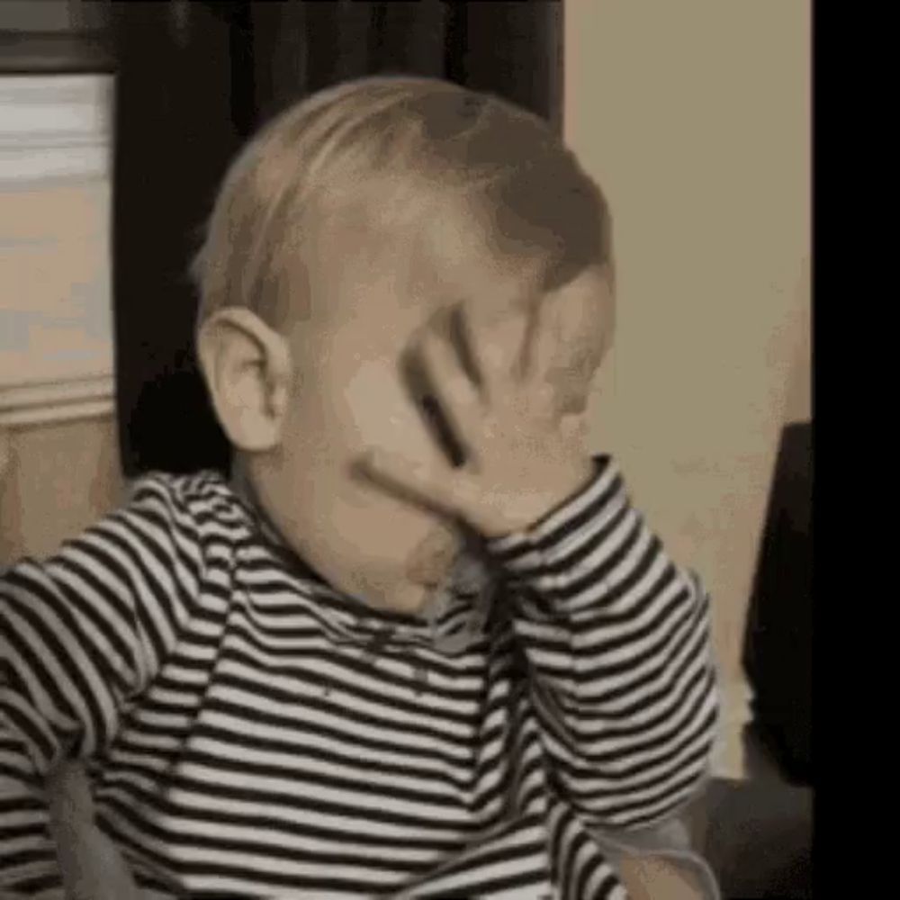 a baby wearing a striped shirt is covering his face with his hand .