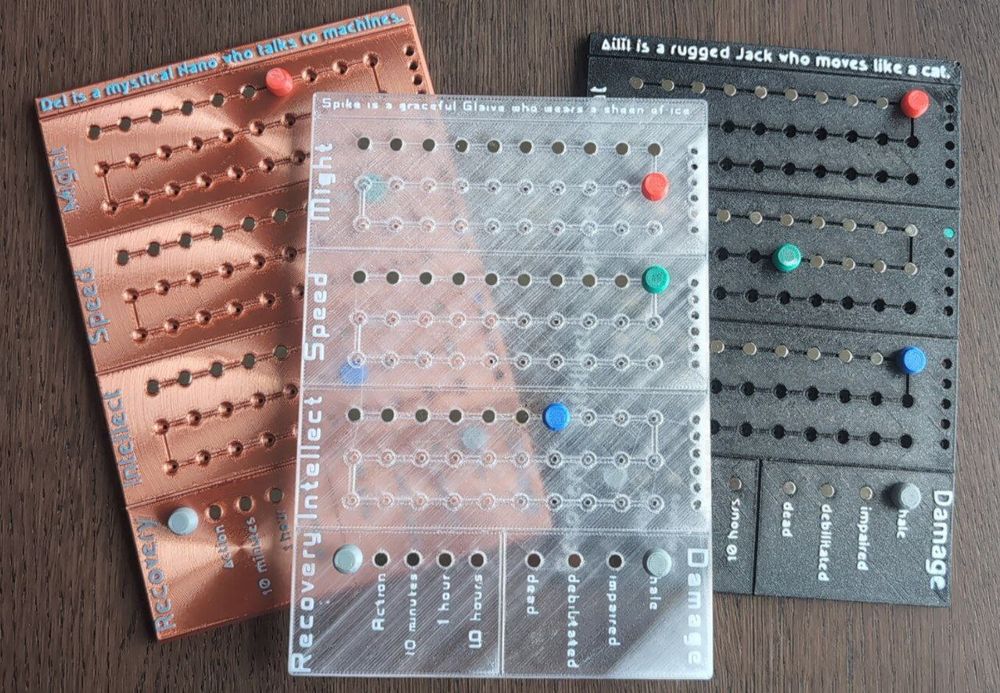 Three 3D-printed gedgets for keeping track of character stats in a Numenera TTRPG campaign. One looks like copper, one is transparent like ice, and one is midnight black.