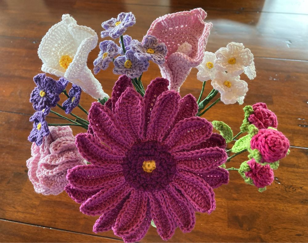 Ein gehäkelter Blumenstrauß in rosa, lila, pink und weiß. Eine große Blume mittig vorne, drumherum dann kleinere.