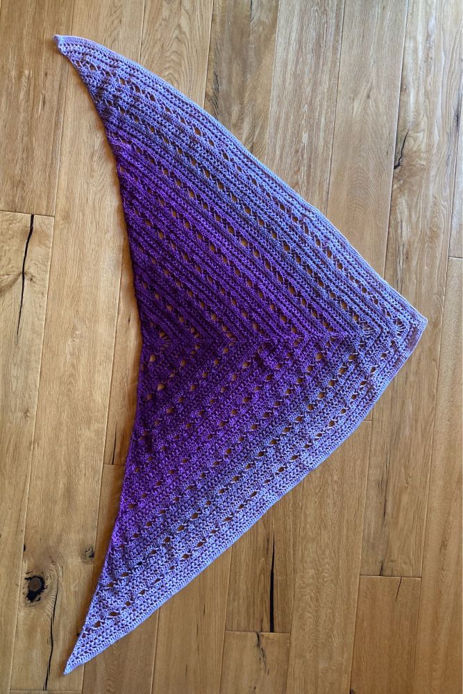 Crocheted triangular shawl in fading purple colors.
