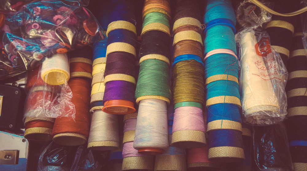 A photo of large spools of thread in a multitude of colours along with vintage measuring tape and buttons