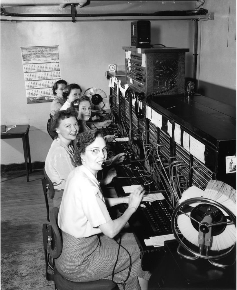Image from the Wikipedia article on switchboard operators (https://en.wikipedia.org/wiki/Switchboard_operator) - a row of women sit in front of an old switchboard. They are wearing headsets and several have cords in their hands, ready to connect calls from the input jacks to the output jacks.