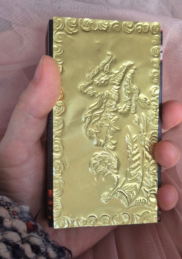 Auf Stanzfolie gestanztes Drachenmotiv mit Ornamenten. Die ich beispielsweise auf eine Streichholzpackung gelegt habe. Anderer Lichteinfall, der die Schatten der Prägefolie anders in Szene setzt.