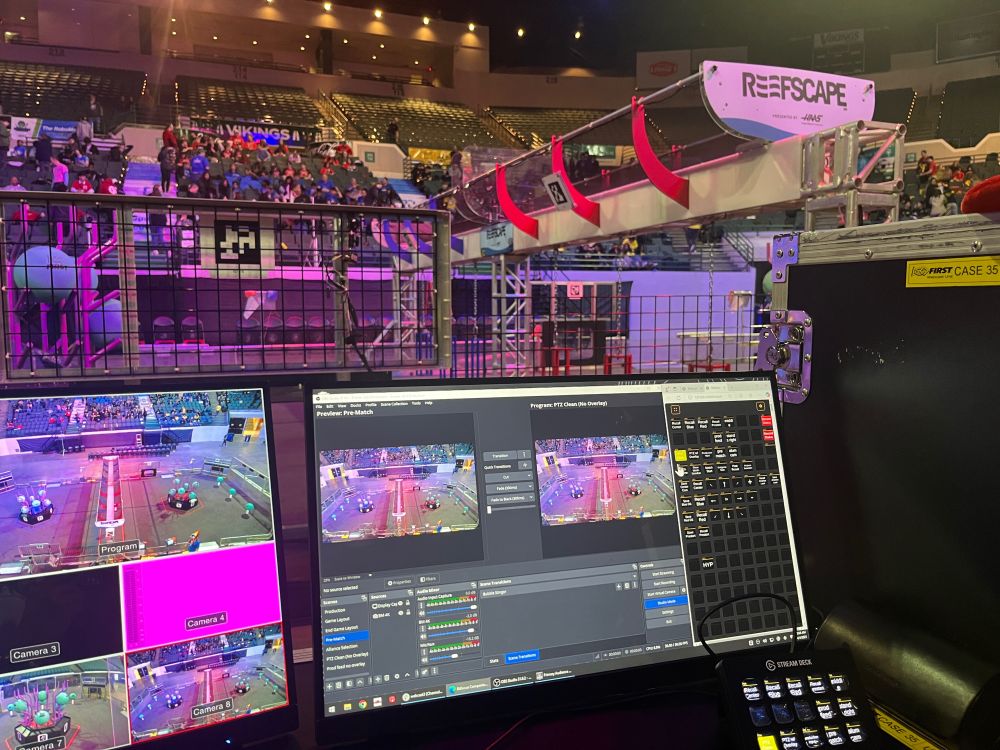 Picture of 2 monitors with broadcast software up, streamdeck, and robotics field in background