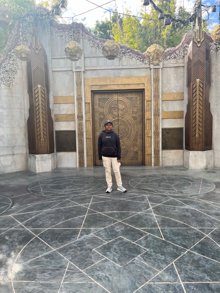 Me wearing a black hat and black hoodie and cargo pants standing in the Doctor Strange Sanctum at Disney California.
