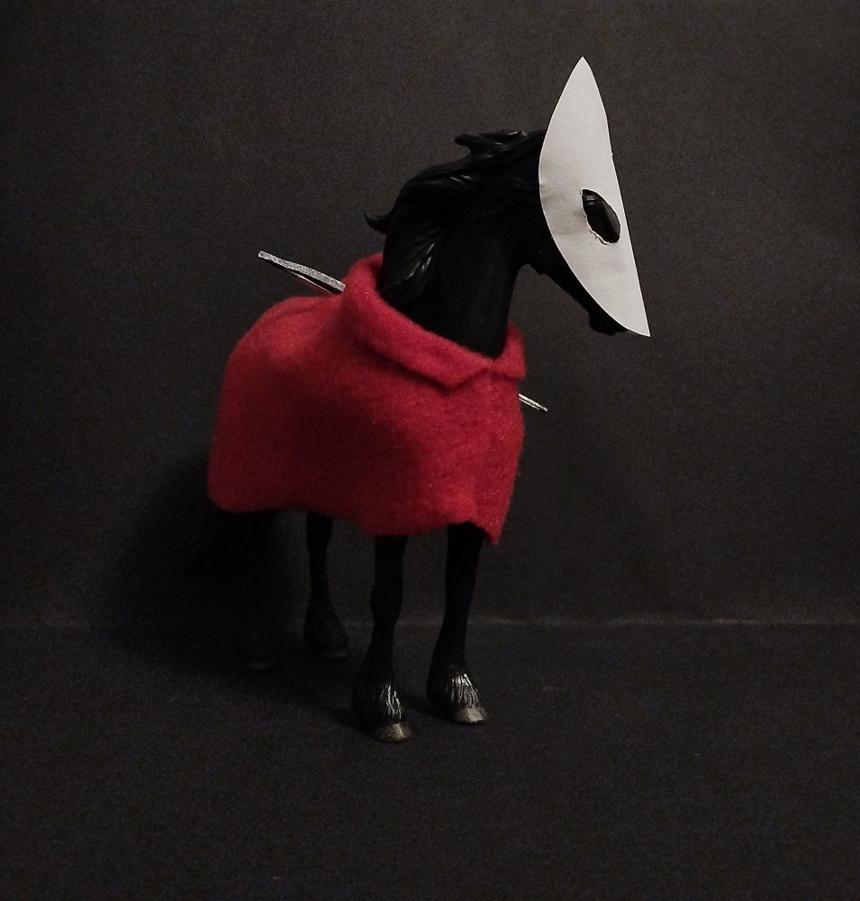 Collecta friesian horse dressed up as Hornet from the game silksong. It has a long white mask with narrow black eyes, and it's wearing a red cloak. It has a big needle as a weapon