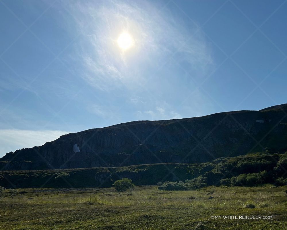 A quiet slope under a high northern sun - the summer light lingers over dark stone and open grass, as if forgetting how to fade.