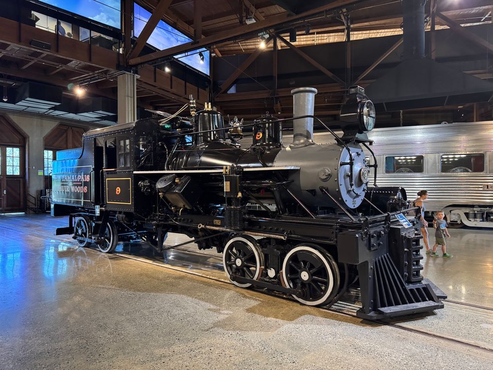 Heisler steam locomotive sits in a roundhouse with a dining car behind it