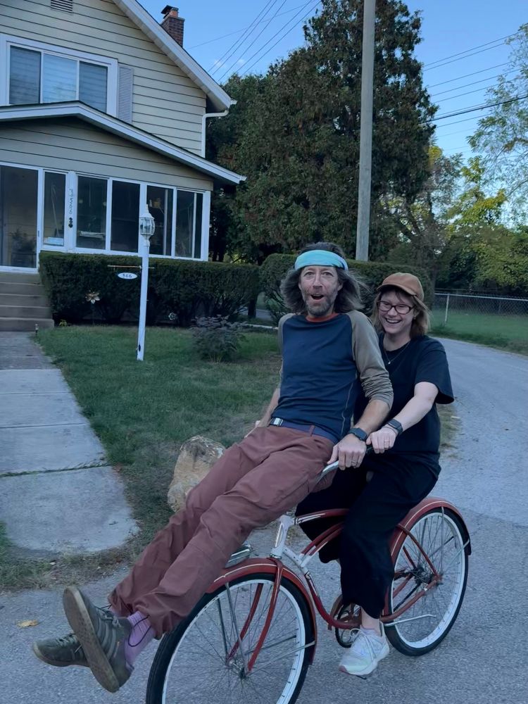 A lady doubles a scoundrel on the handlebars of her ancient cruiser bike