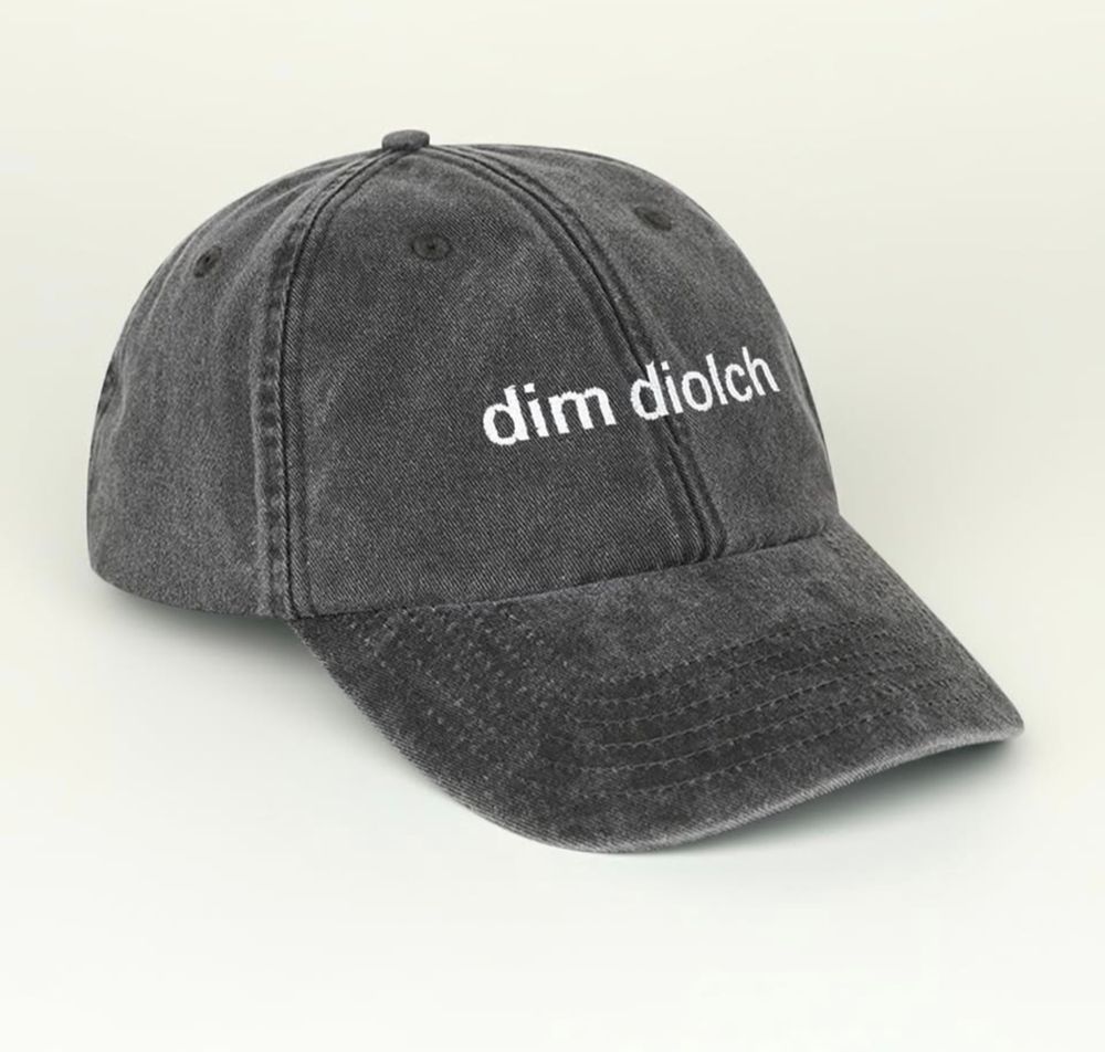 A grey baseball cap with the words 'dim diolch' printed on it. 
