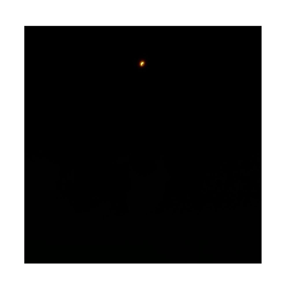 Photo of a partial-coverage solar eclipse. It resembles an orange crescent moon in a featureless black sky