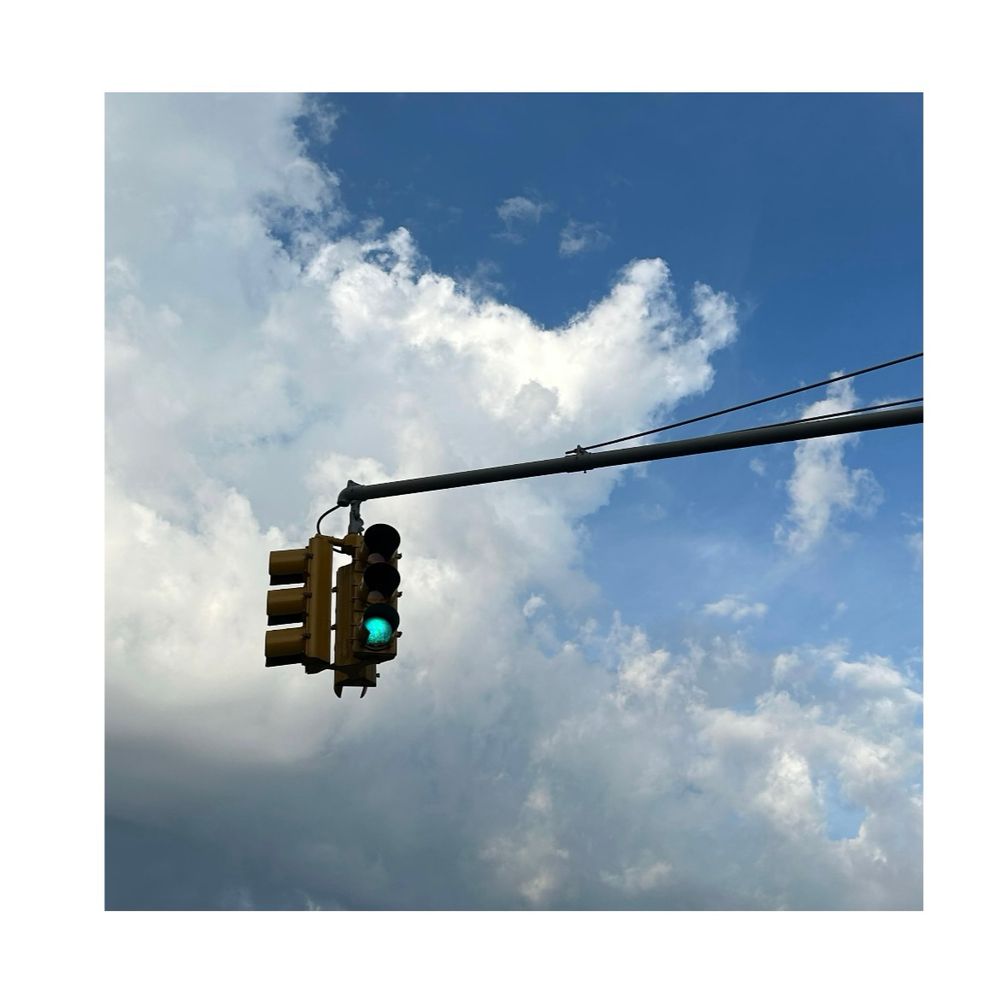 A stoplight set to green in front of a partly cloudy sky