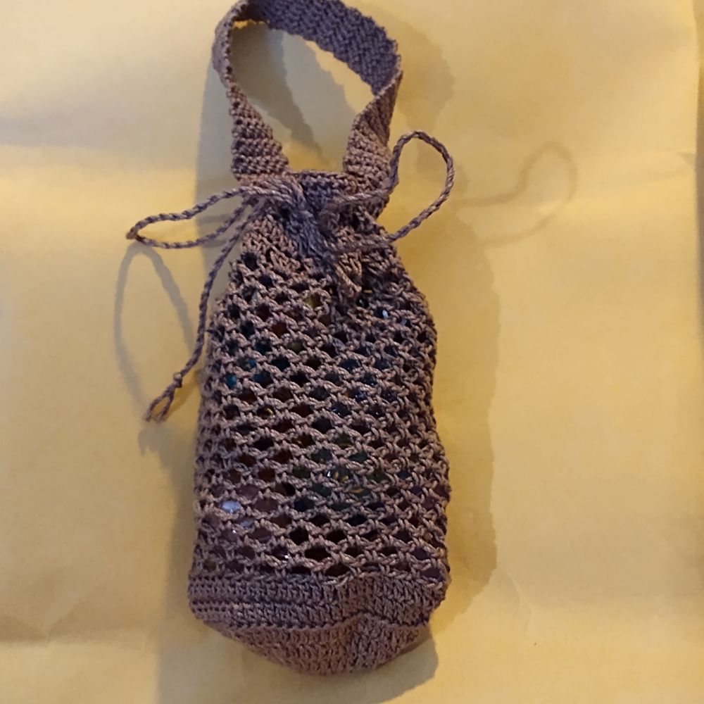 Light brown crochet net bag lying on its side with 22 dice in it, background is yellow. Bag has carry handle and drawstring closure.