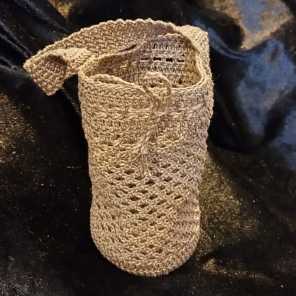 Light brown crochet net bag on a black background. Bag has carry handle and drawstring closure.